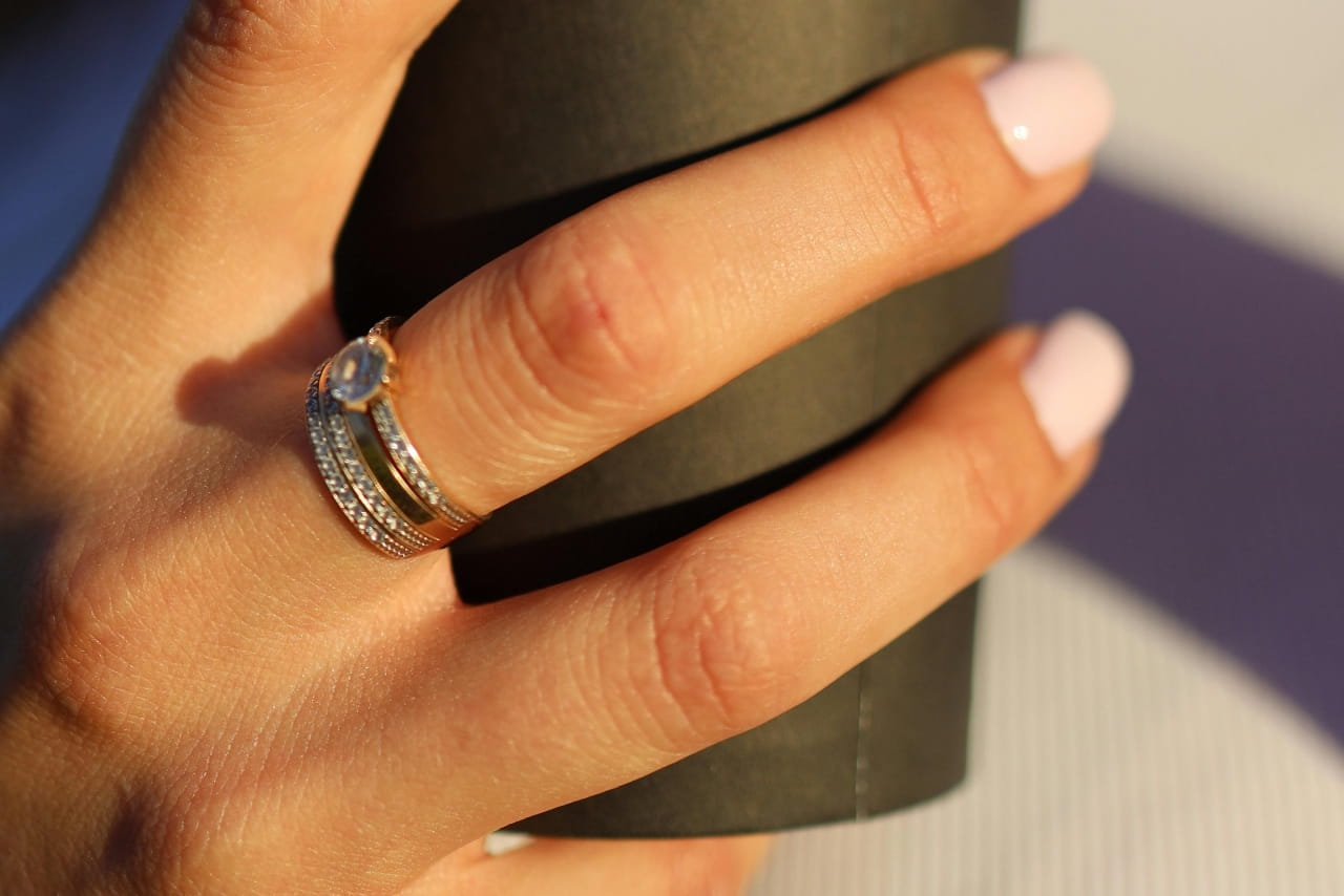 A woman with a side stone engagement ring, a gold wedding band, and diamond anniversary bands while she holds a black coffee cup in a close-up shot.