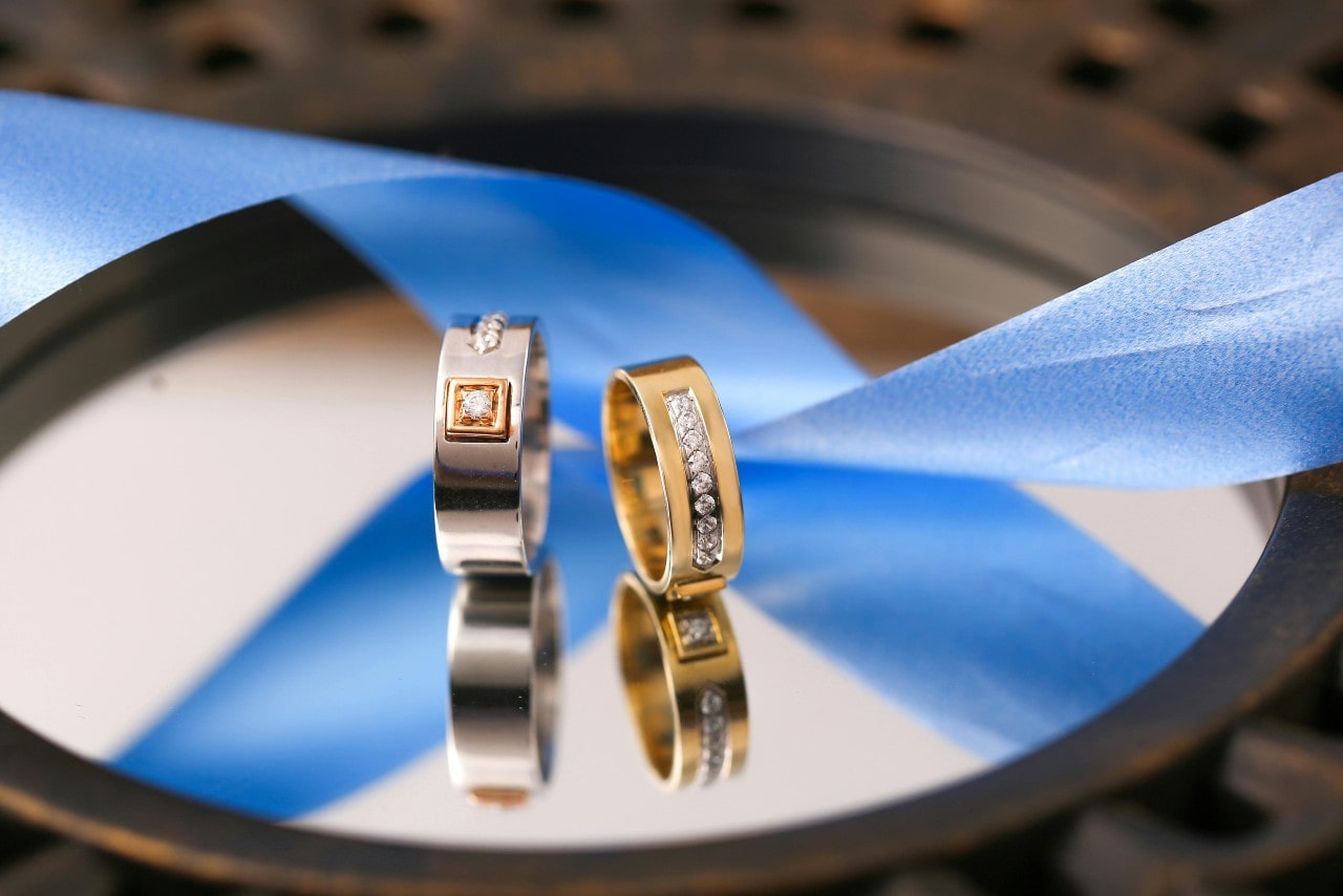 Two diamond wedding rings resting on a mirror with a blue ribbon reflection.