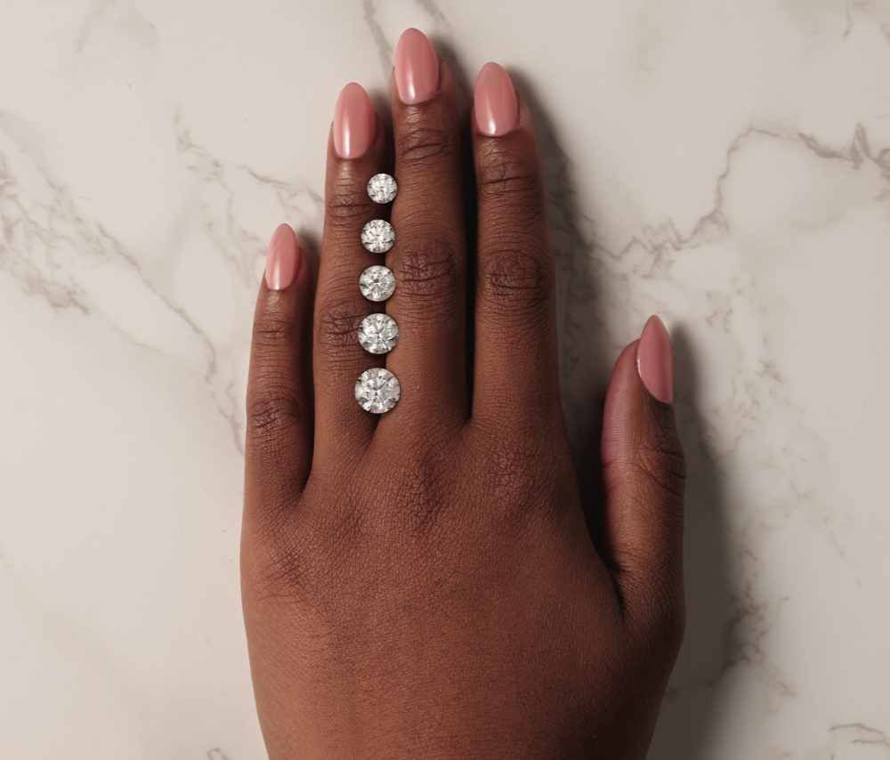 A row of different size round diamonds resting on a woman’s hand in-between