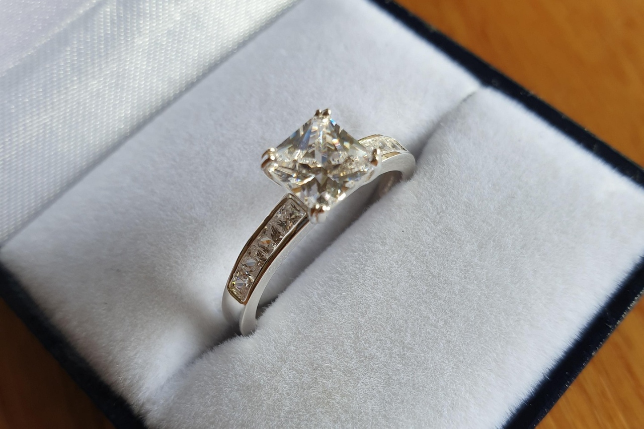 A close-up of a white gold side stone engagement ring with a princess cut center diamond displayed in its box.