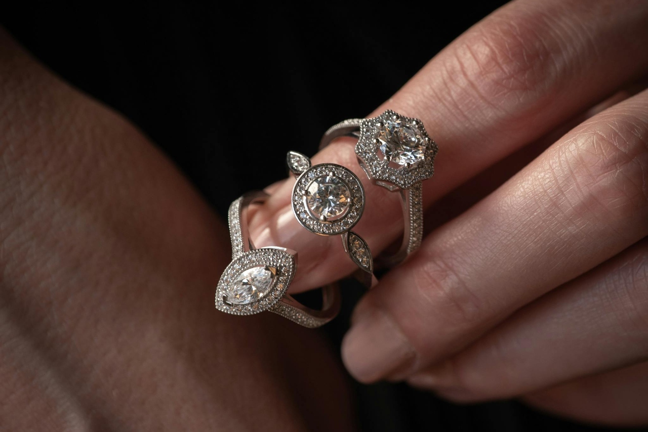 A detailed close-up of three vintage-inspired diamond rings worn on a hand, featuring marquise, round, and floral halo designs with intricate pavé settings and sparkling gemstones. A detailed close-up of three vintage-inspired diamond rings worn on a hand, featuring marquise, round, and floral halo designs with intricate pavé settings and sparkling gemstones.