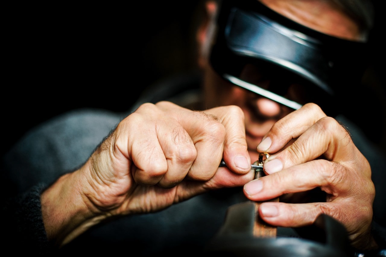A close up of a jeweler in a helmet fixing a yellow gold ring with a tool.