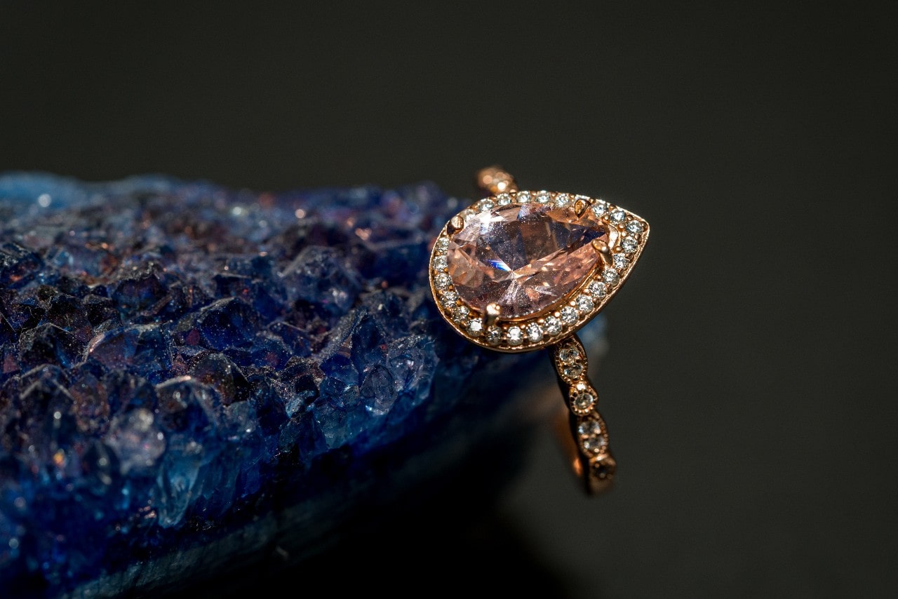 A beautiful pear-shaped sapphire ring with a diamond halo rests on rough blue crystal. A beautiful pear-shaped sapphire ring with a diamond halo rests on rough blue crystal.