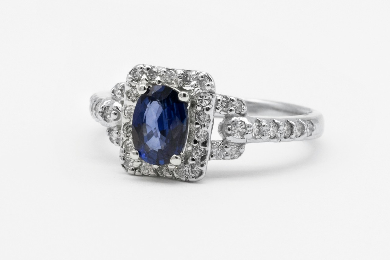 A white gold engagement ring featuring an oval-cut blue sapphire center stone surrounded by a halo of diamonds, set against a white background A white gold engagement ring featuring an oval-cut blue sapphire center stone surrounded by a halo of diamonds, set against a white background